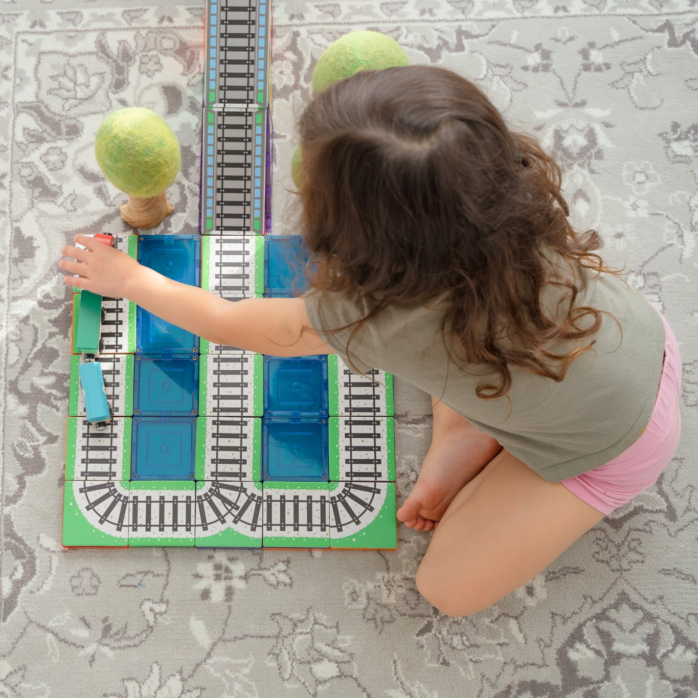 Child playing with Train Pack toppers, magnetic tiles and wooden trees