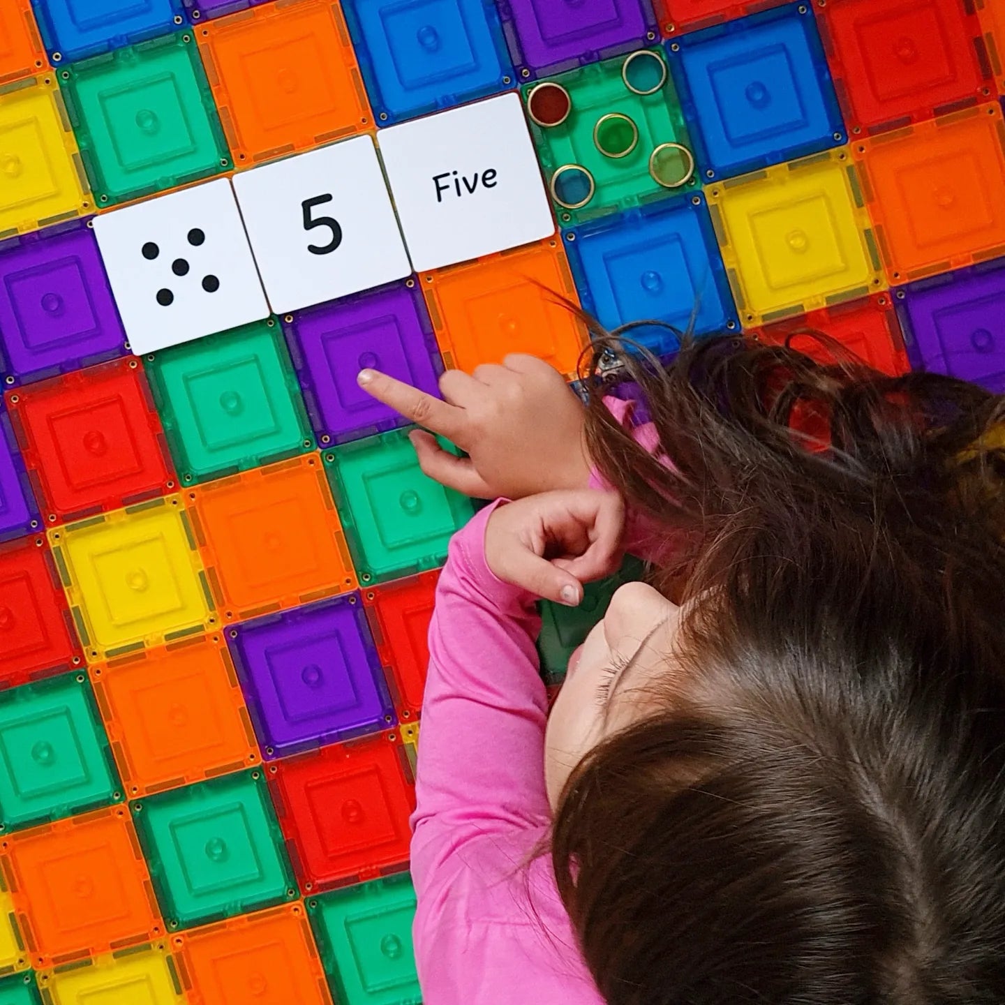 Child pointing to number 5 with the Numbers Pack toppers on rainbow tiles