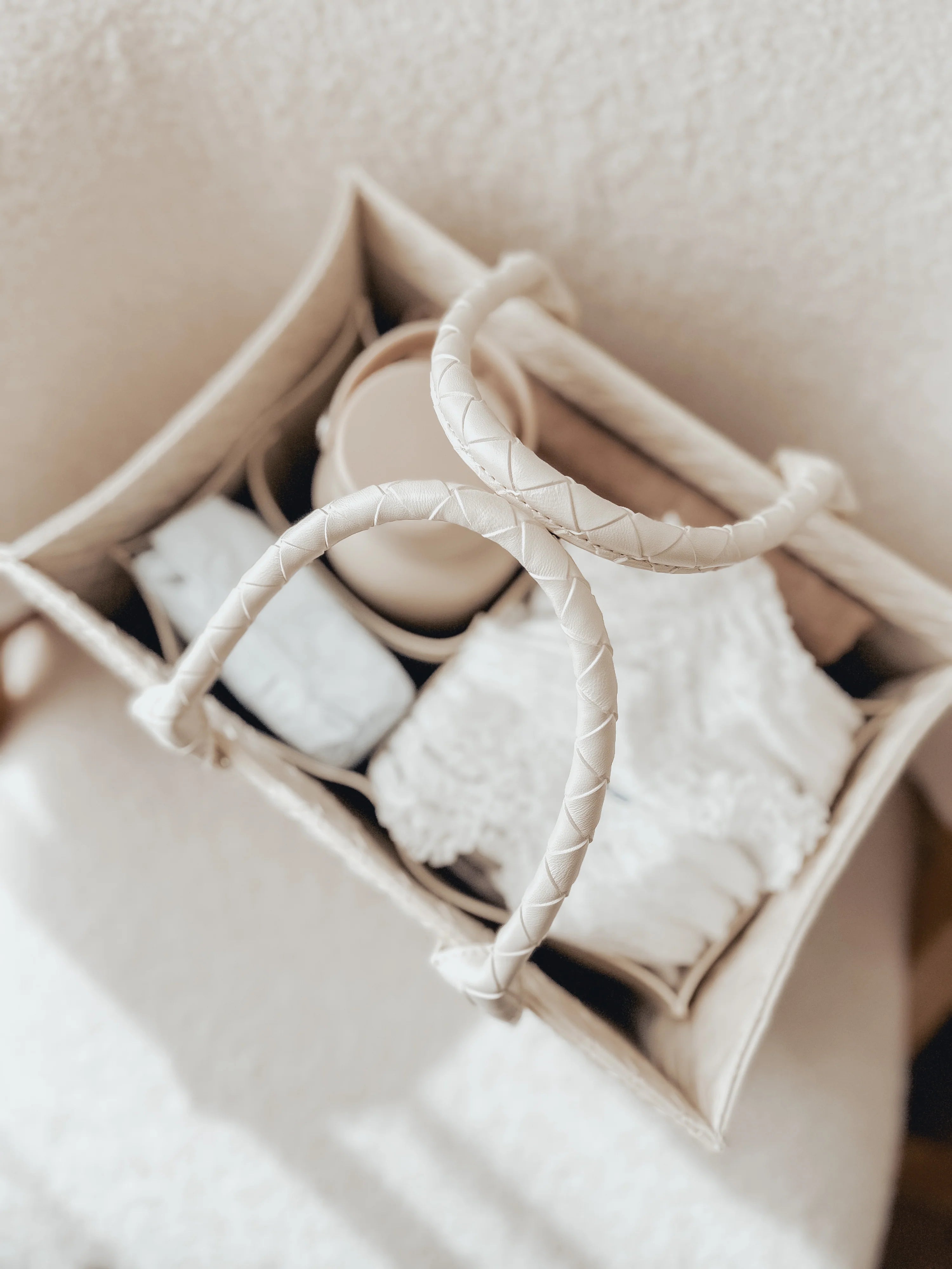 Baby items including a white blanket, gray socks, and a beige hat in a white basket on a light background.