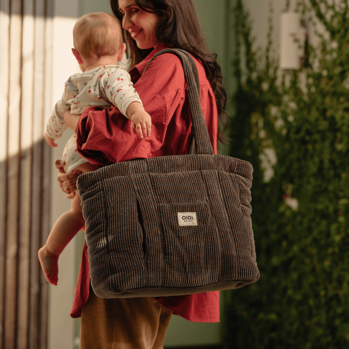 Parent carrying the OiOi Everyday Tote nappy bag while holding a baby