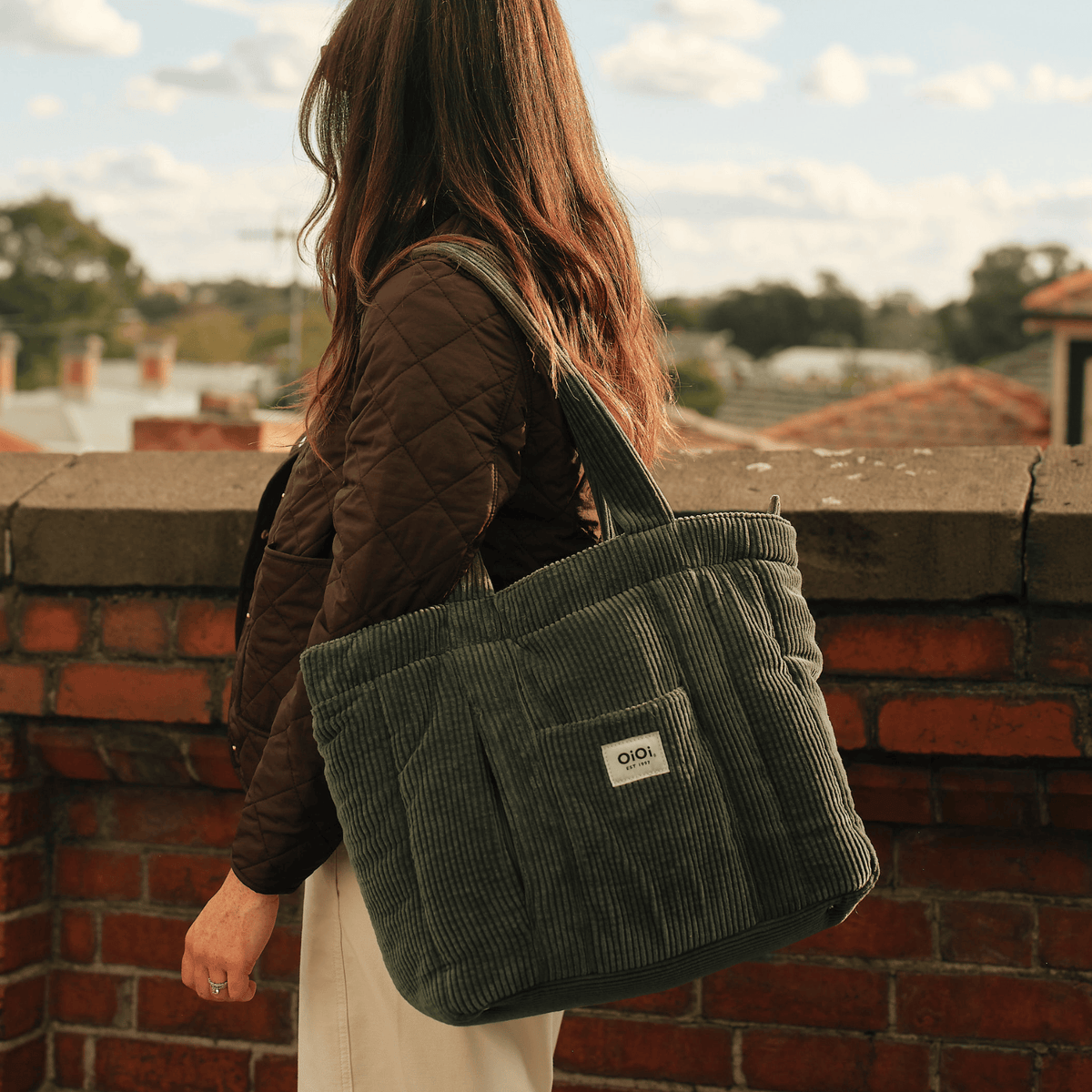 OiOi Everyday Tote nappy bag in moss green clipped to a pram with the included stroller straps