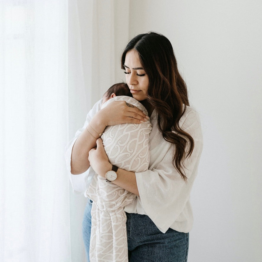 Mother holding a newborn swaddled in the Te Patiki Pepi Wrap in Mocha