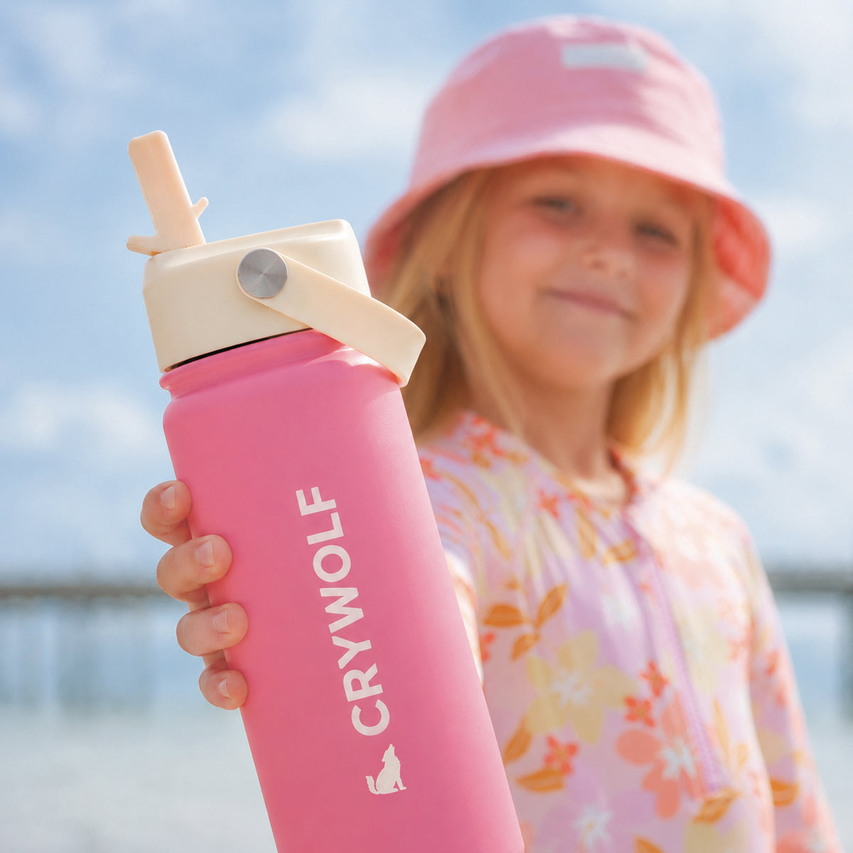 Child holding the Crywolf 545ml drink bottle in Hibiscus pink at the beach