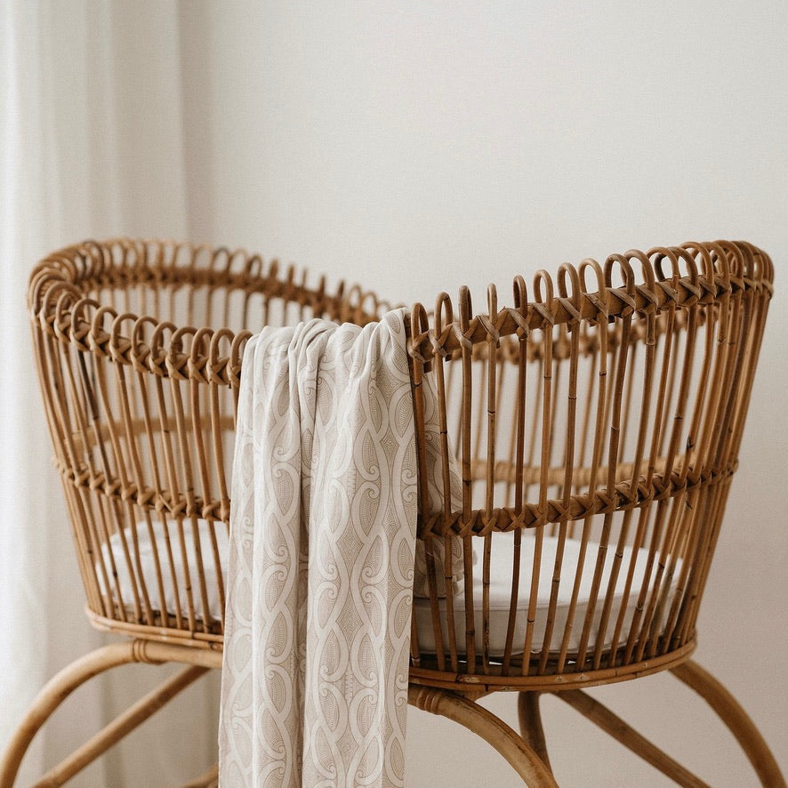 Te Patiki Pepi Wrap in Mocha draped over a rattan bassinet