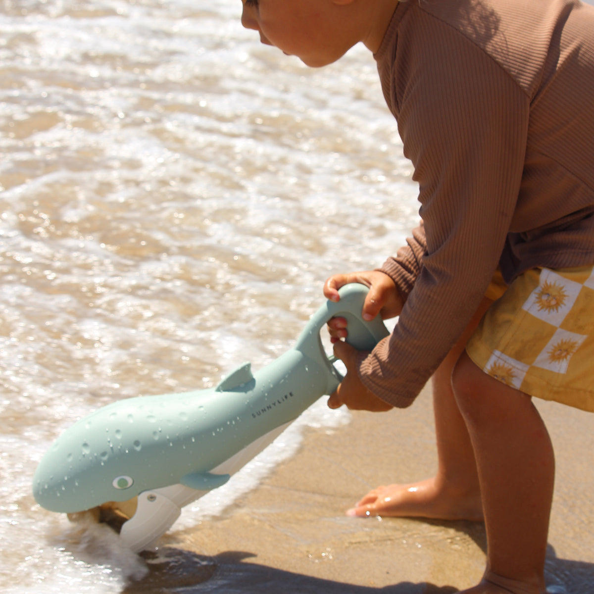 Child scooping sand with the Sunnylife Sand Claws Whale at the beach