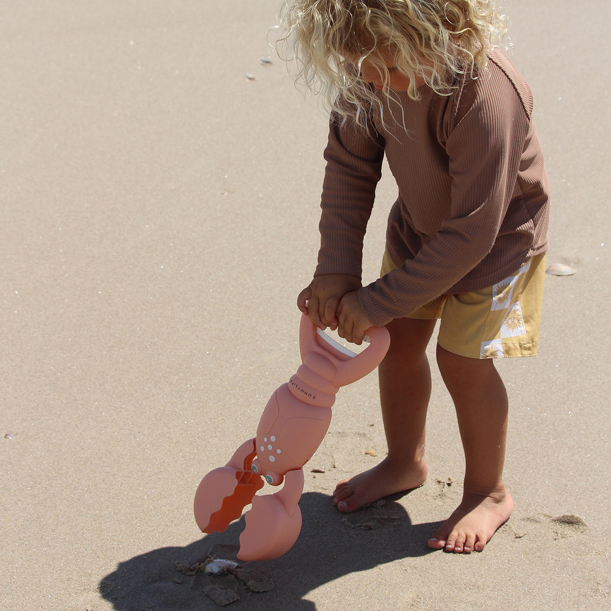 Child scooping sand with the Sunnylife Sand Claws Lobster at the beach