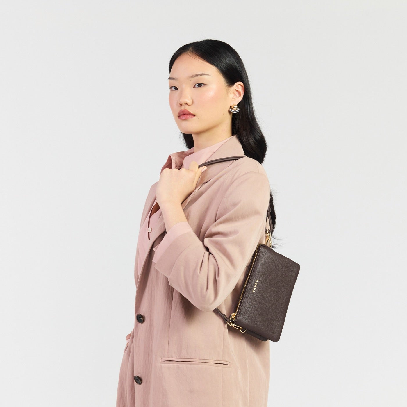 Woman wearing a pink suit with a matching handbag on a light gray background
