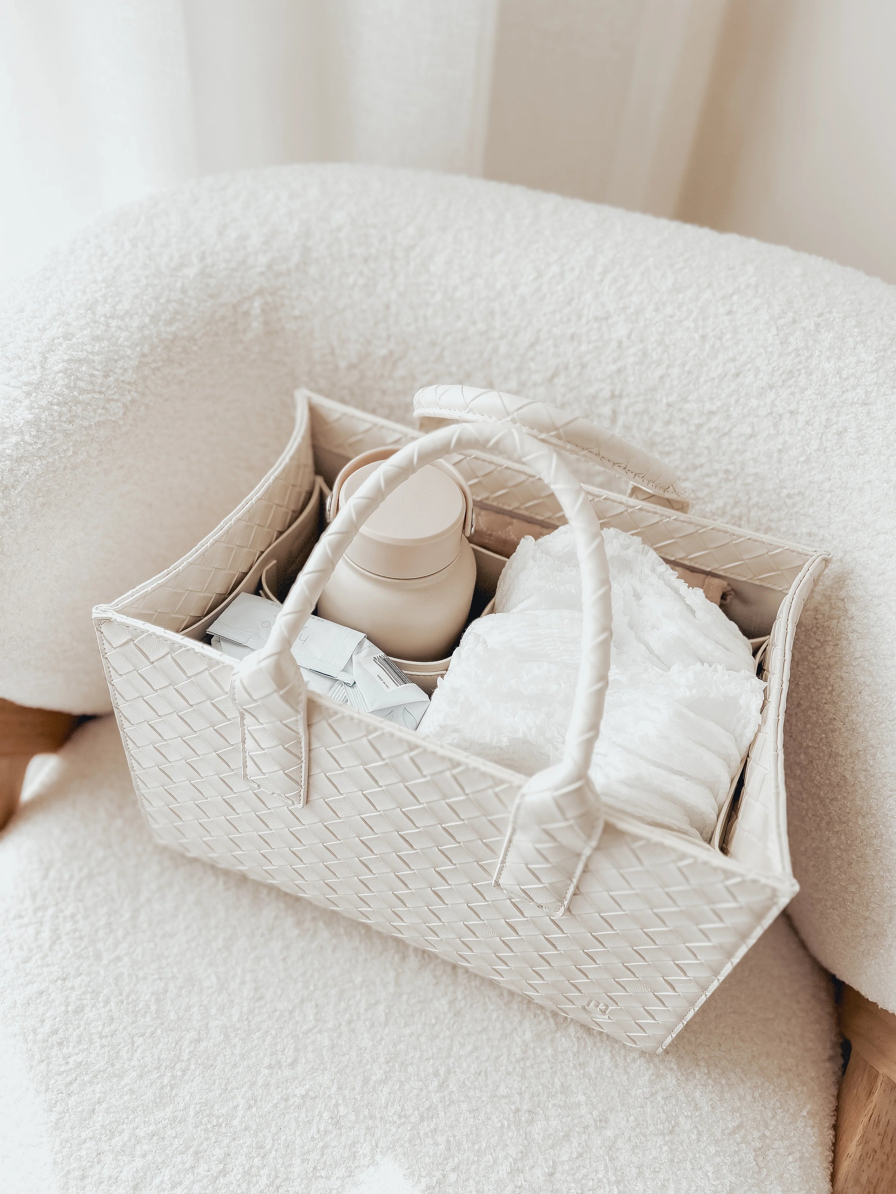 White woven basket with baby shoes and items on a soft surface