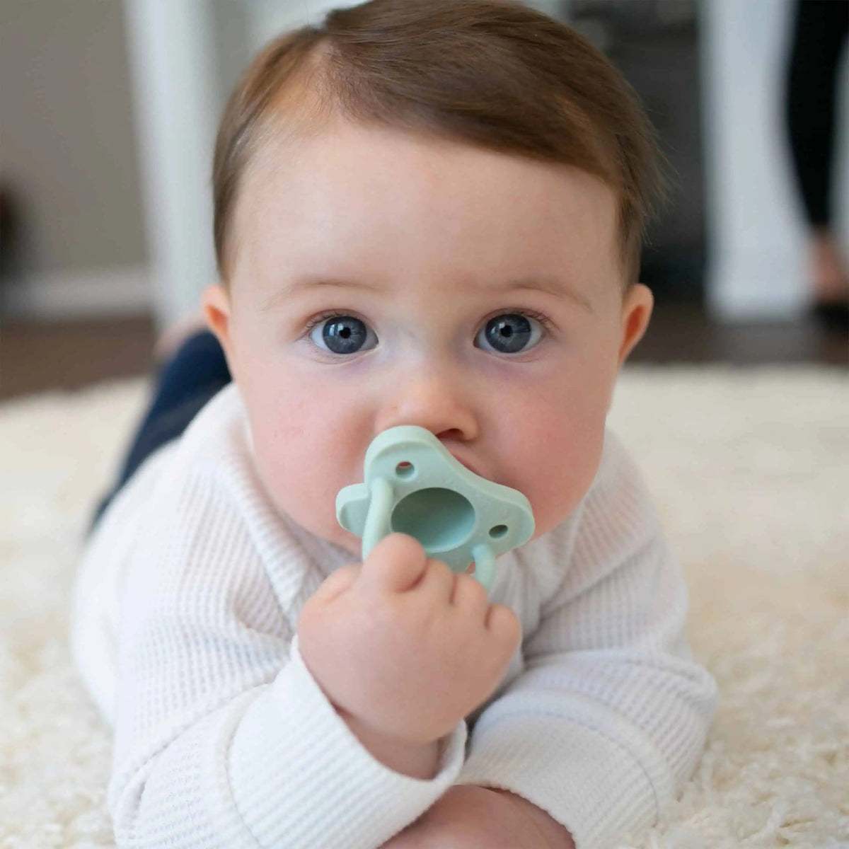 Baby holding a green Dr Brown's HappyPaci silicone soother