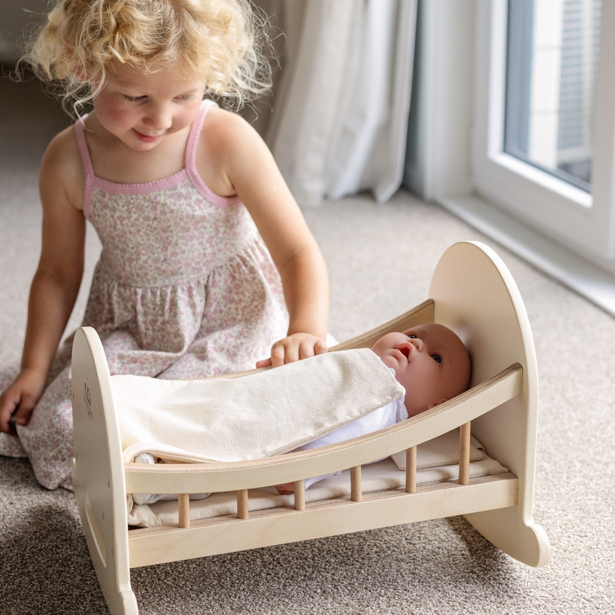 Child tucking a doll into the Kinderfeets Doll Crib