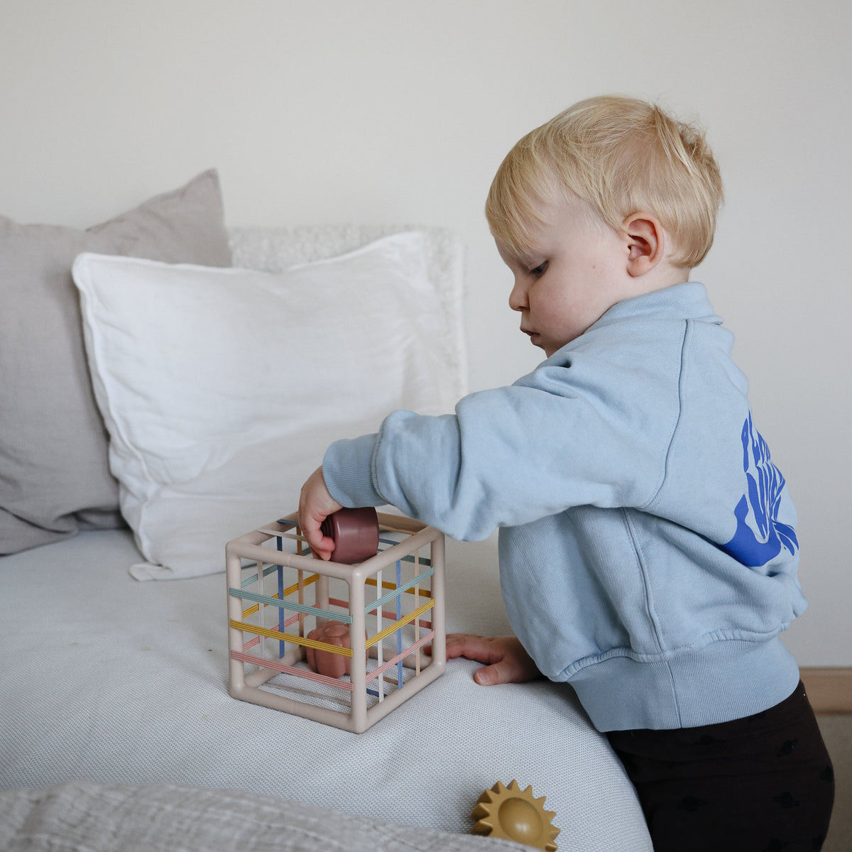 Toddler fitting shapes into the Mushie Elastic Shape Sorter